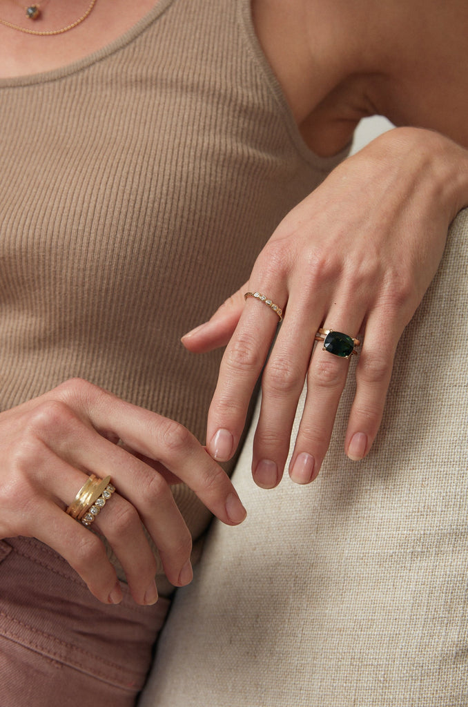 woman wearing gold ring with four prong cushion cut sapphire alongside other gold jewelry