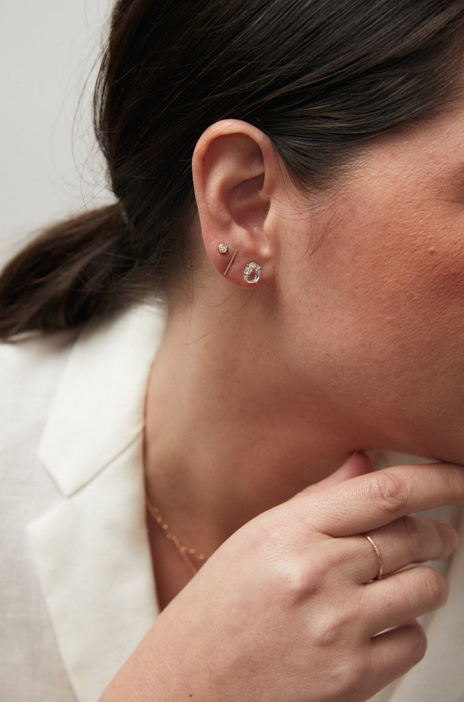 close up of woman wearing gold oval aquamarine stud alongside other gold jewelry