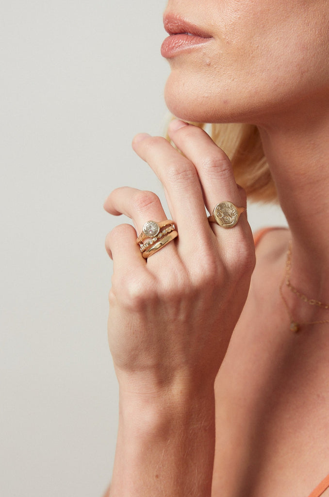 gold ring with bezel set round salt + pepper diamond on woman's hand alongside other gold rings