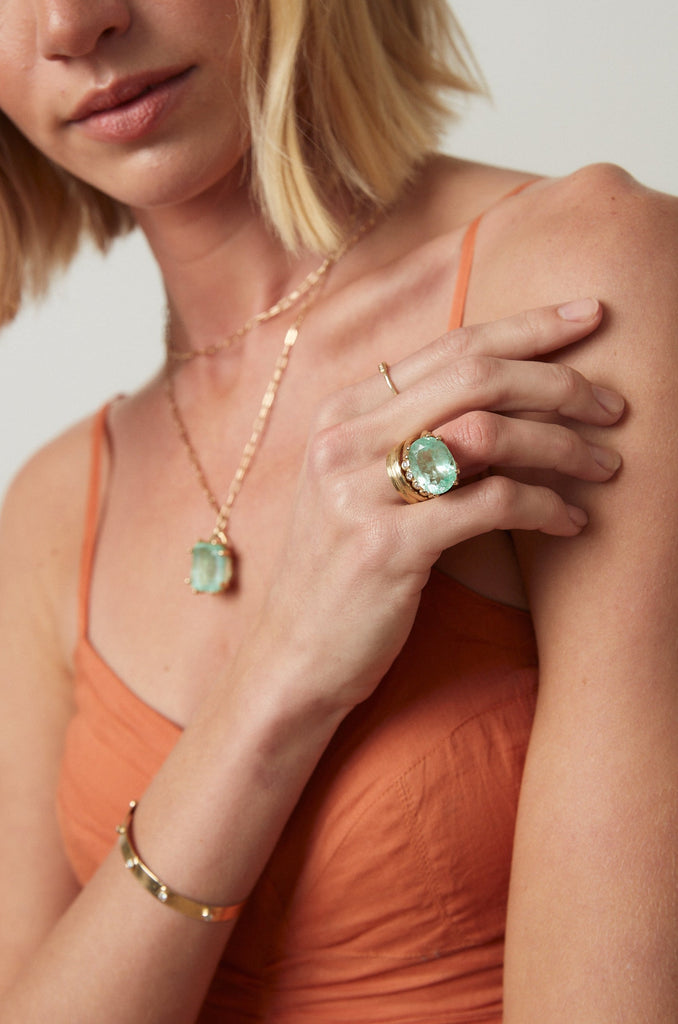 woman wearing gold 8 prong ring with oval colombian emerald alongside other gold jewelry