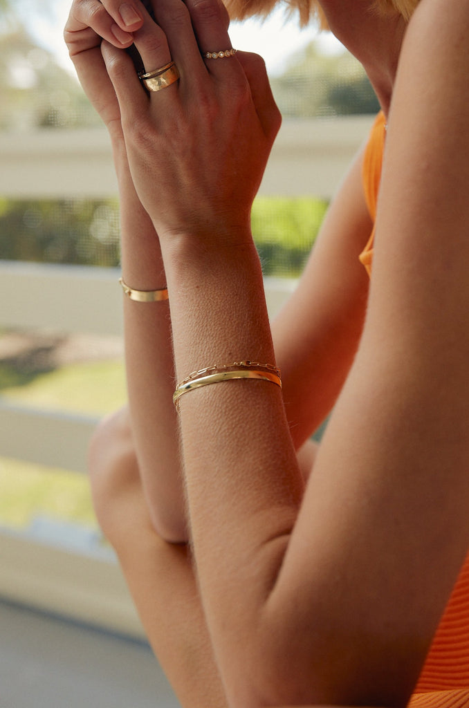 woman wearing gold cable chain bracelet alongside two bracelets and three gold rings