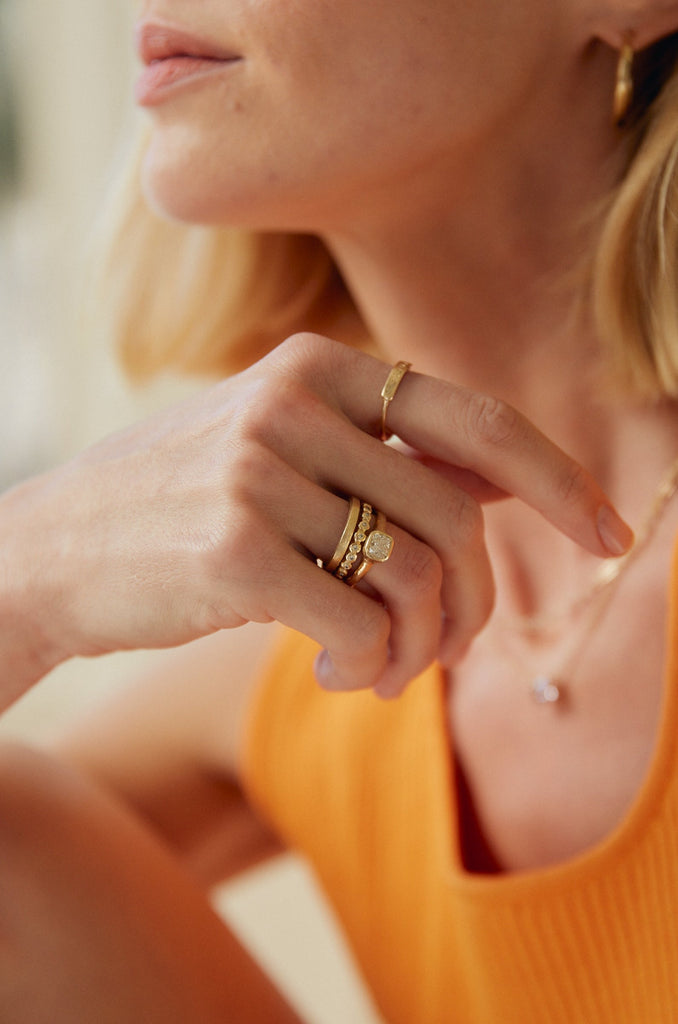 woman wearing gold band with bezel set round white diamonds alongside other gold rings