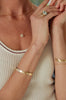 close up of woman wearing gold cuff bracelet studded with diamonds alongside other gold jewelry