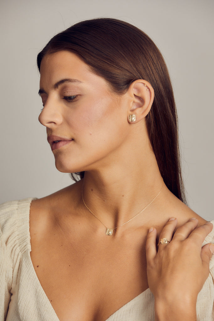 woman wearing free form gold square studs with baguette white diamond alongside other gold jewelry