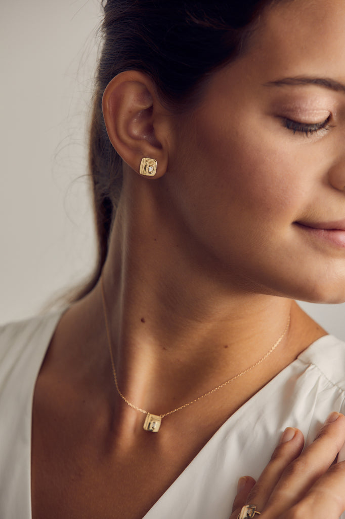 woman wearing free form gold square studs with baguette white diamond alongside matching necklace