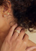 close up of woman wearing gold eternity band with bezel set round diamonds alongside other gold jewelry