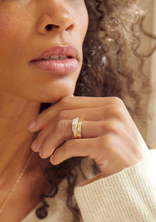 close up of woman wearing gold band with straight sides alongside other gold ring