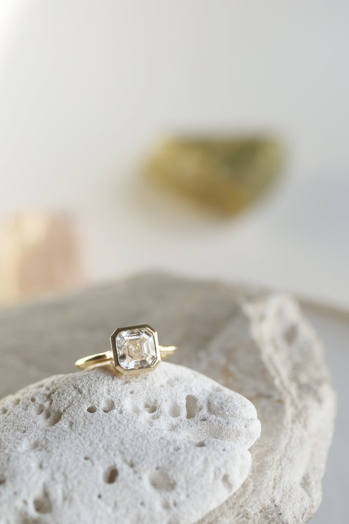 close up of gold ring with bezel set asscher cut white diamond