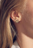 close up of woman wearing free form gold square studs with baguette white diamond alongside other gold earring