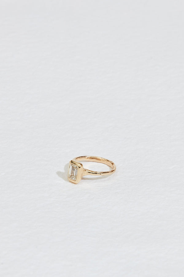 side view of gold ring with bezel set emerald cut white diamond