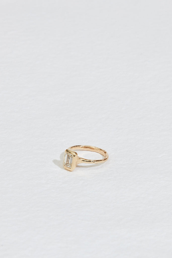side view of gold ring with bezel set emerald cut white diamond
