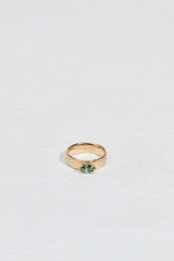 close up of wide gold band with blue green pear diamond