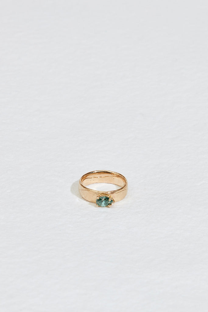 close up of wide gold band with blue green pear diamond