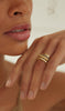 close up of woman wearing gold ring with angular face alongside other gold rings