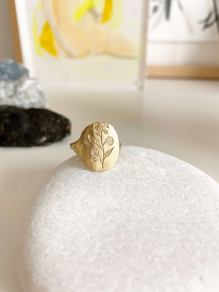 close up of gold signet ring with engraved flower on rock