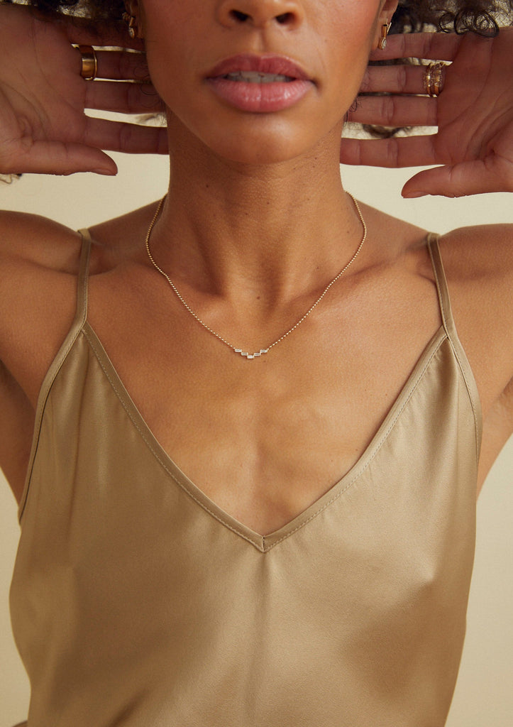 woman wearing gold ball chain necklace with five baguette cut stair step diamonds alongside other gold jewelry