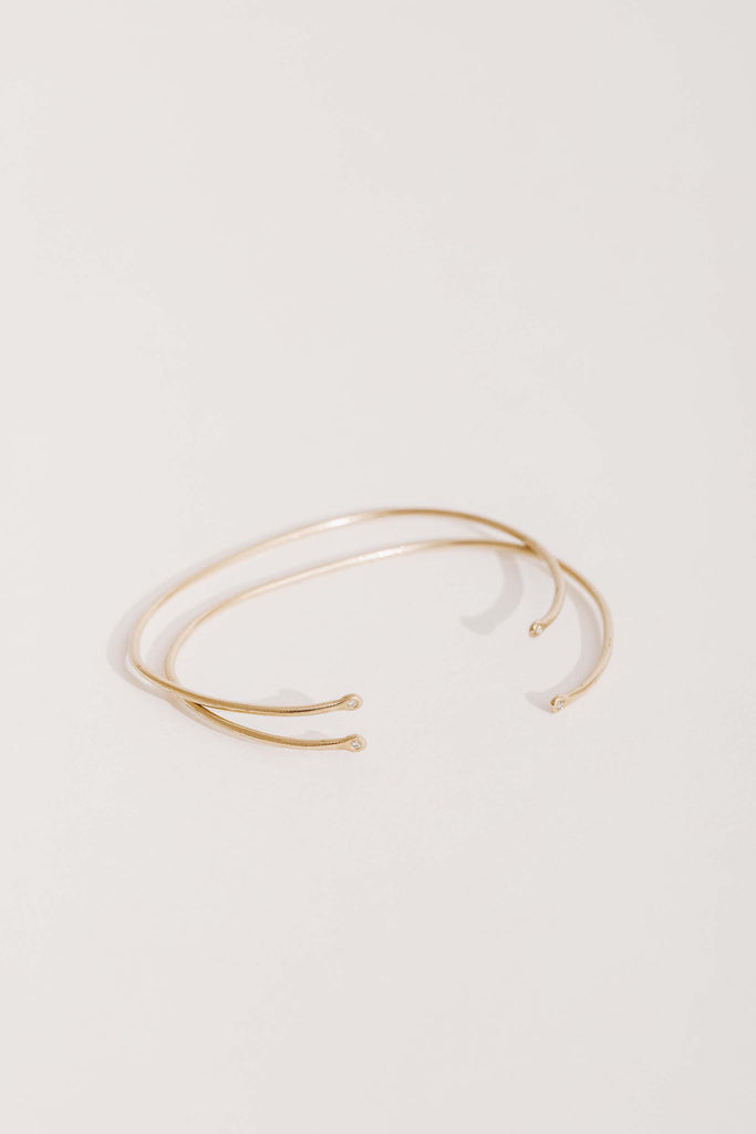 side view of two thin gold cuffs with small round diamonds on ends