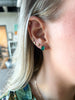 close up of woman wearing gold emerald cut emerald stud alongside other gold earrings