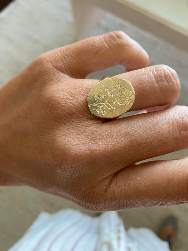 close up of gold signet ring with engraved flowers on hand