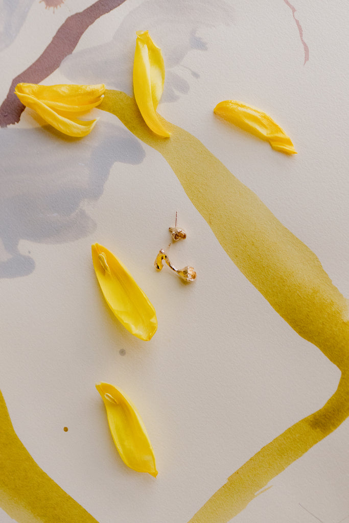 gold tulip stud alongside tulip petals and other jewelry