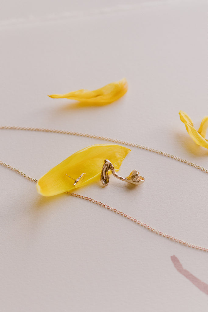 gold tulip stud alongside tulip petals and other gold jewelry