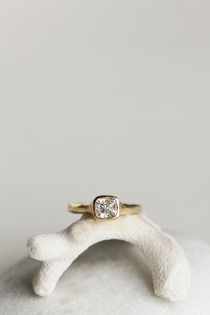 close up of gold ring with cushion cut bezel set white diamond