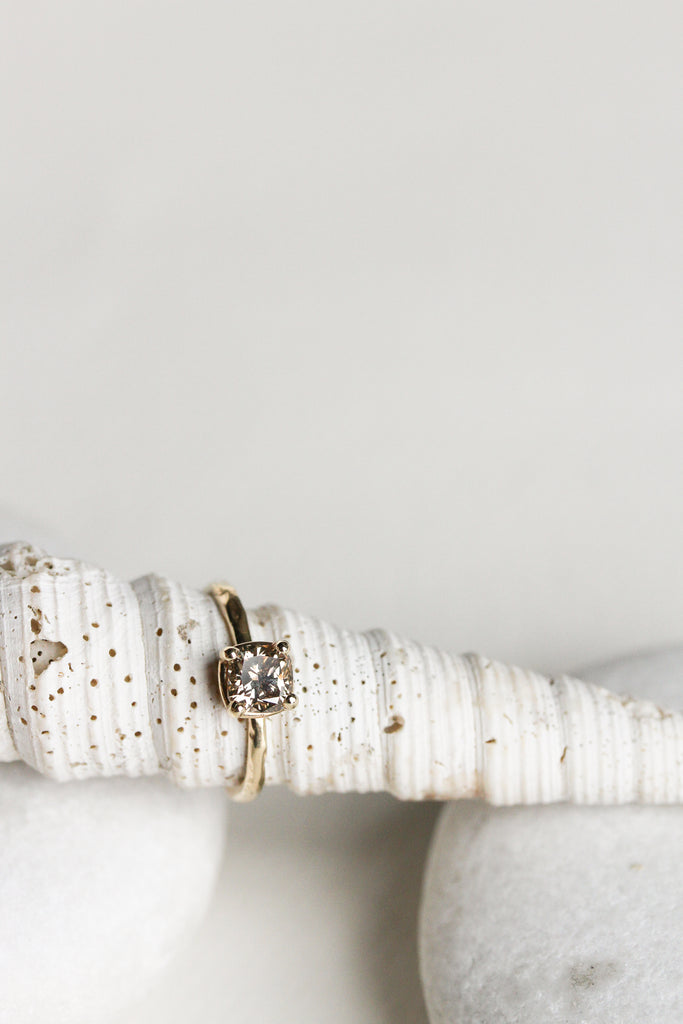 close up of gold four prong ring with cushion cut light champagne diamond