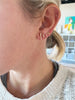 close up of woman wearing gold tube shaped studs alongside other gold earrings