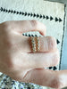 close up of hand wearing gold ring with five bezel set round white diamonds alongside other gold band