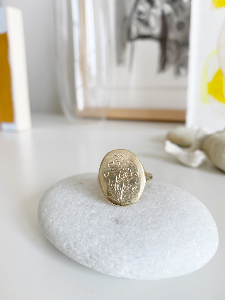 close up of gold signet ring with engraved flowers on rock