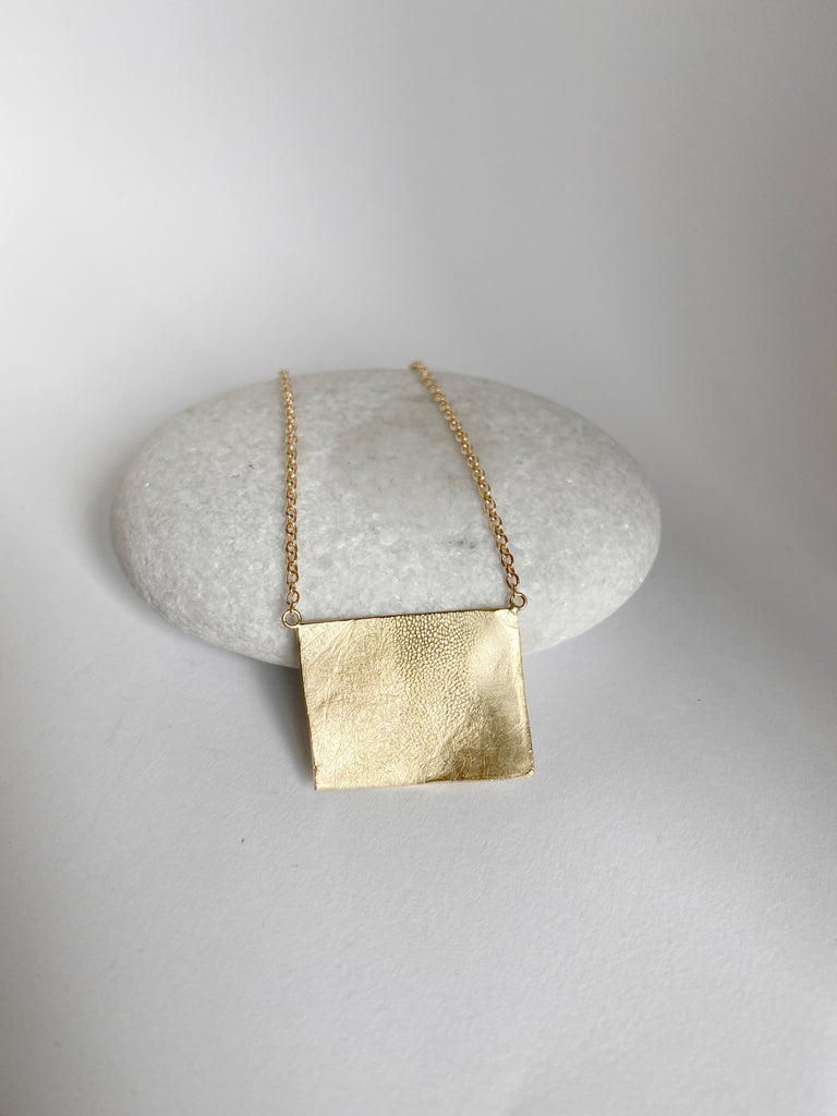 close up of gold necklace with engraved dog print bar