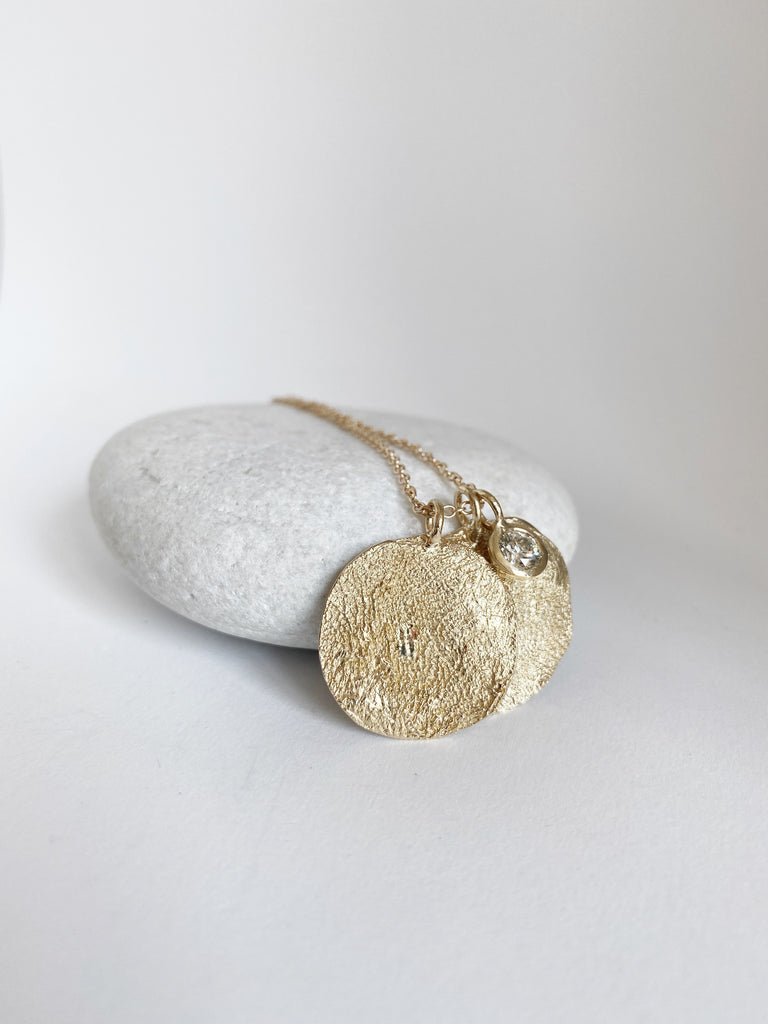 close up of gold necklace with two engraved dog print discs and bezel set round diamond