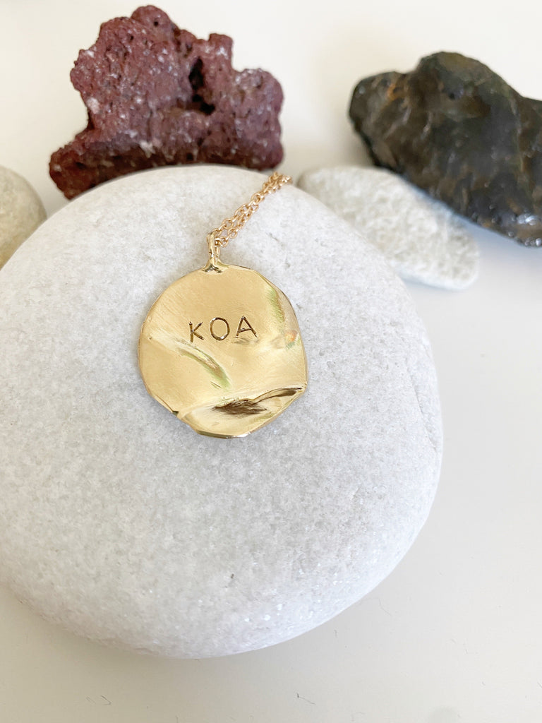 close up of gold disc necklace with engraved name