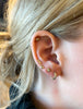 close up of woman wearing gold semi hoop earring with five bezel set round white diamonds alongside other gold earrings