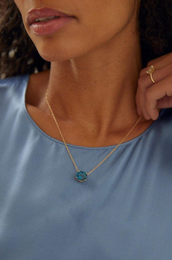 close up of woman wearing gold necklace with oval blue topaz