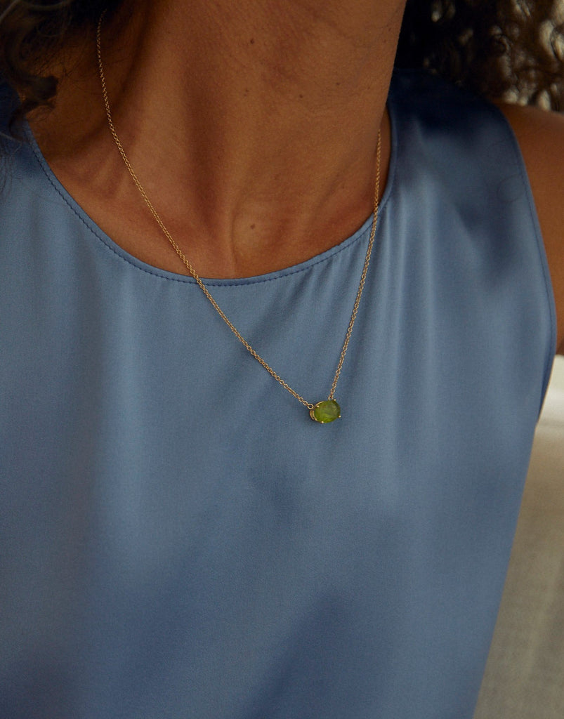 close up of woman wearing gold necklace with oval peridot