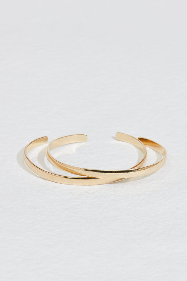 close up of two gold cuff bracelets with rounded edges