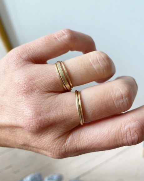 close up of hand wearing thin gold band with straight sides alongside other gold rings