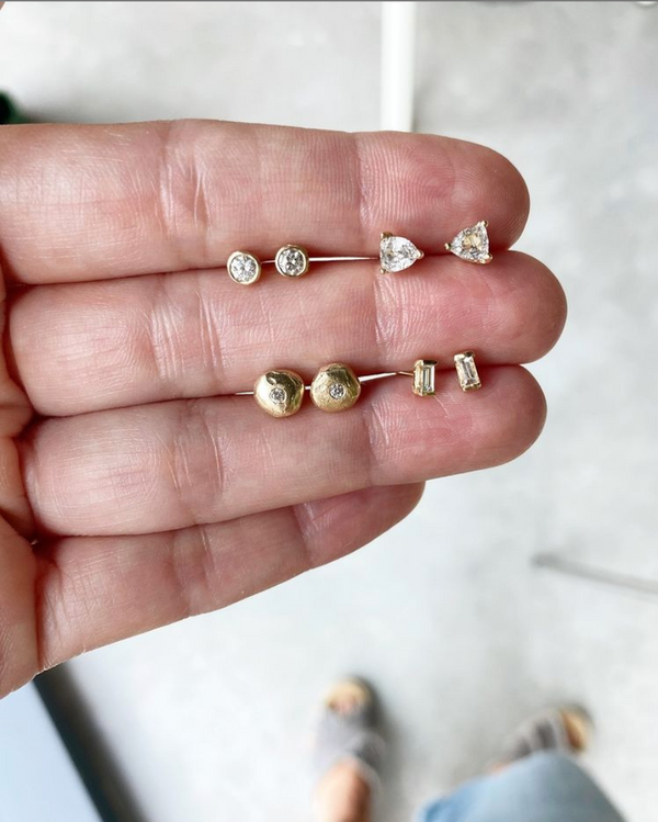 close up of hand holding bezel set round white diamond gold studs alongside other gold studs