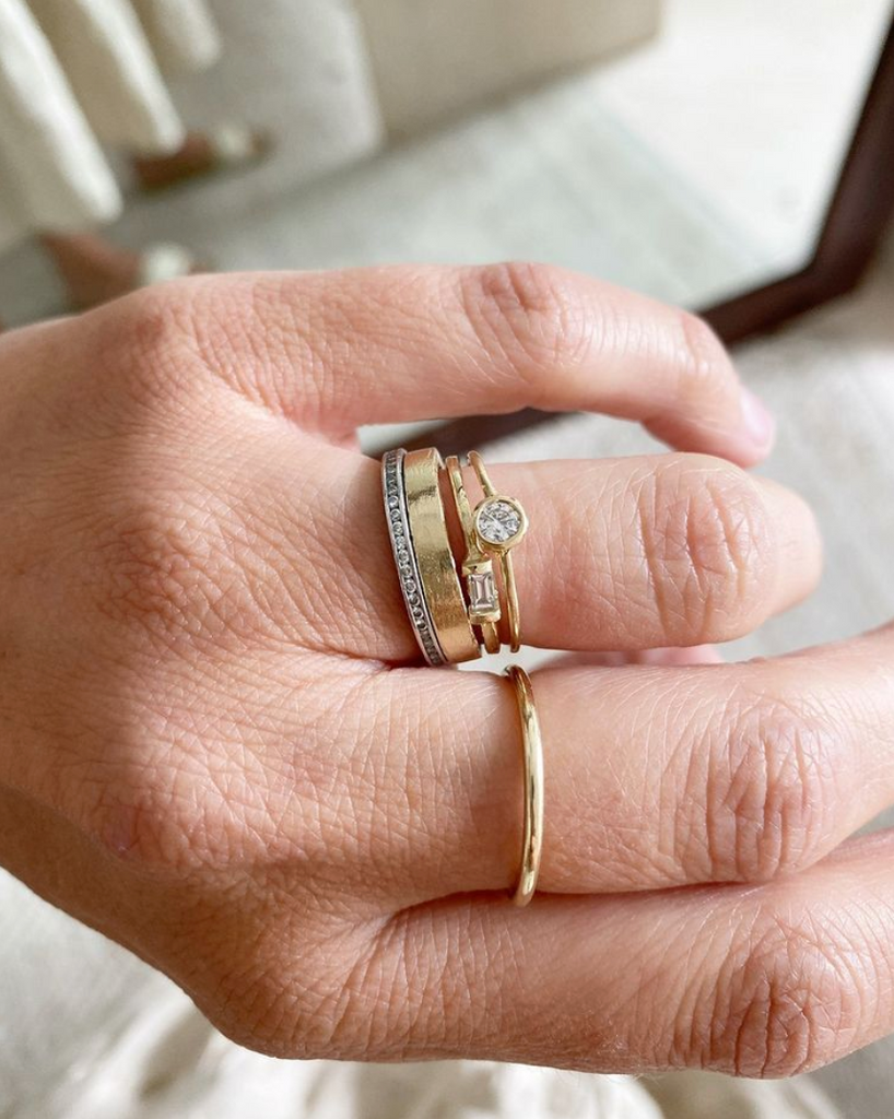close up of hand wearing gold band with white baguette diamond alongside other rings