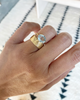 close up of hand wearing gold four prong oval aquamarine ring with textured band alongside cigar band