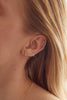 close up of woman wearing gold tube shaped stud alongside other gold earrings