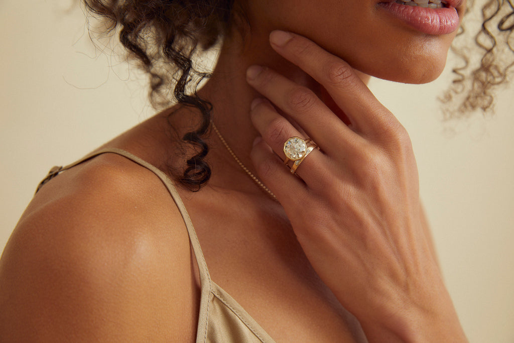 close up of woman wearing gold ring with decagon bezel set round brilliant diamond alongside gold band