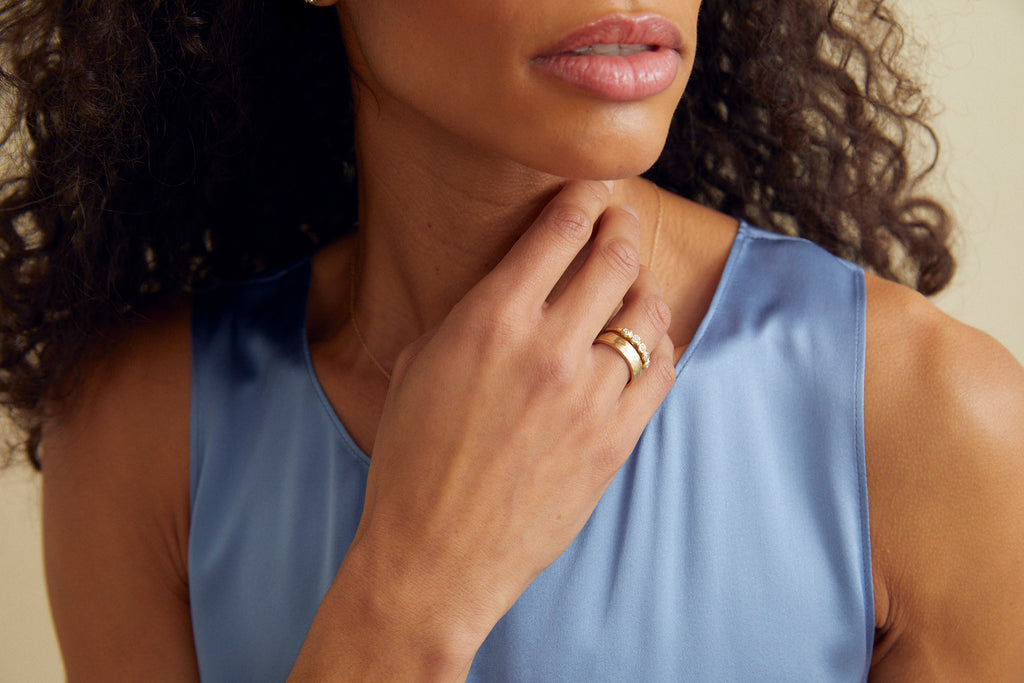 woman wearing moderately textured gold band with straight sides alongside other gold ring