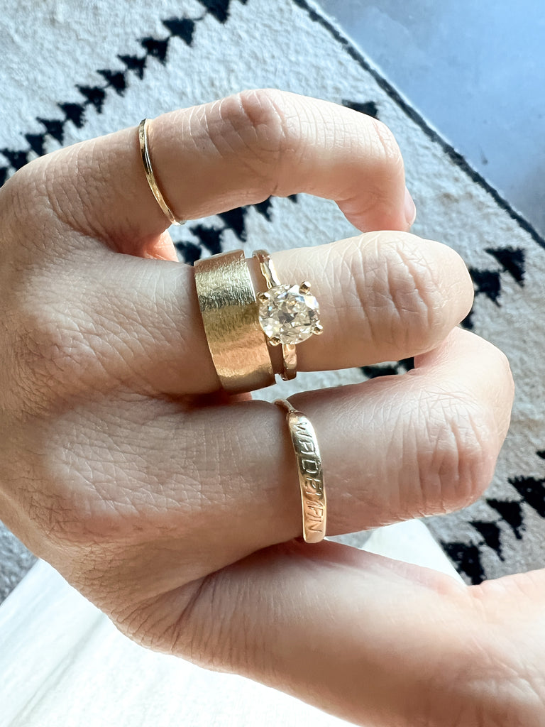 close up of hand wearing gold four prong ring with old european cut round white diamond alongside other gold rings