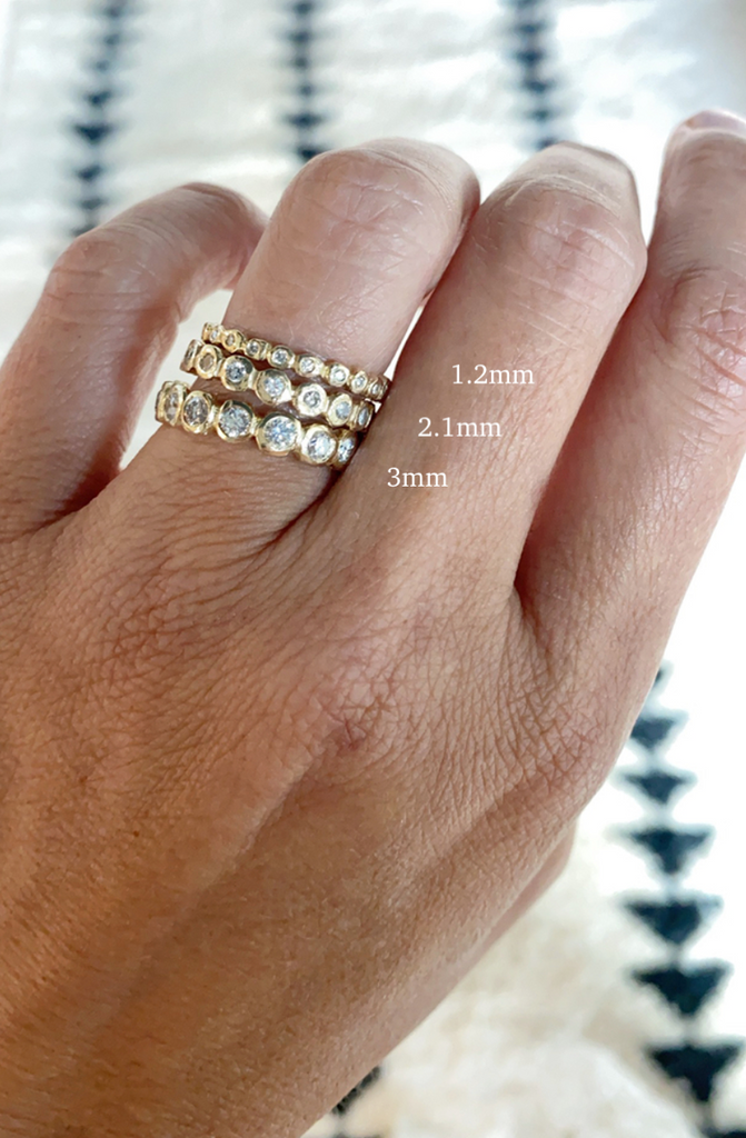 close up of hand wearing three sizes of gold band with bezel set round white diamonds