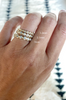close up of hand wearing gold eternity band with bezel set round diamonds alongside other eternity bands