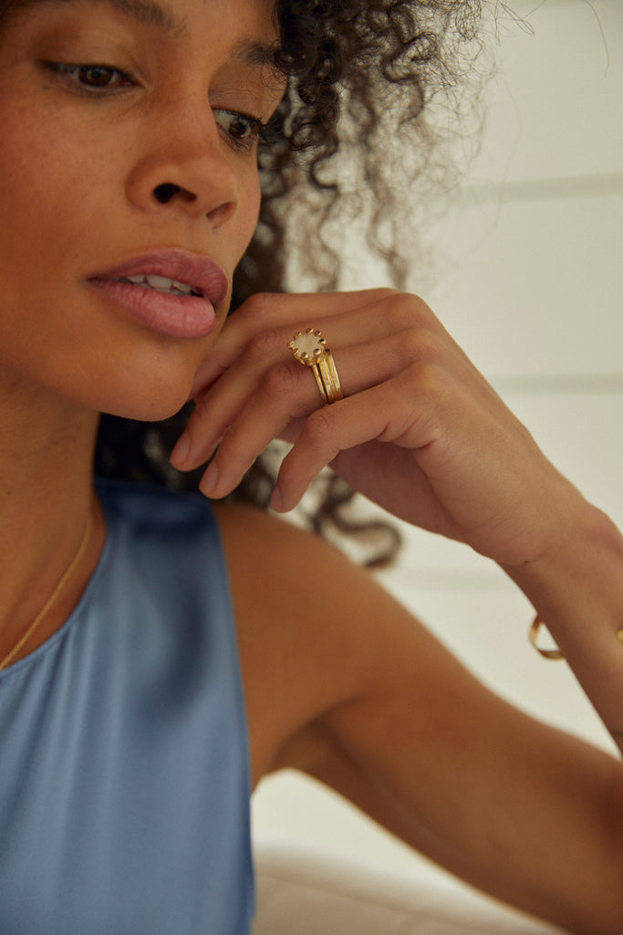 woman wearing gold moderately textured band with notch in center alongside other gold ring