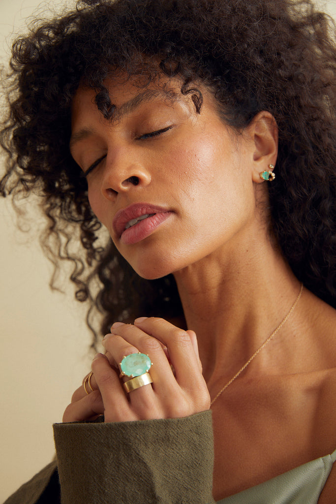 woman wearing gold 8 prong ring with oval colombian emerald alongside other gold jewelry