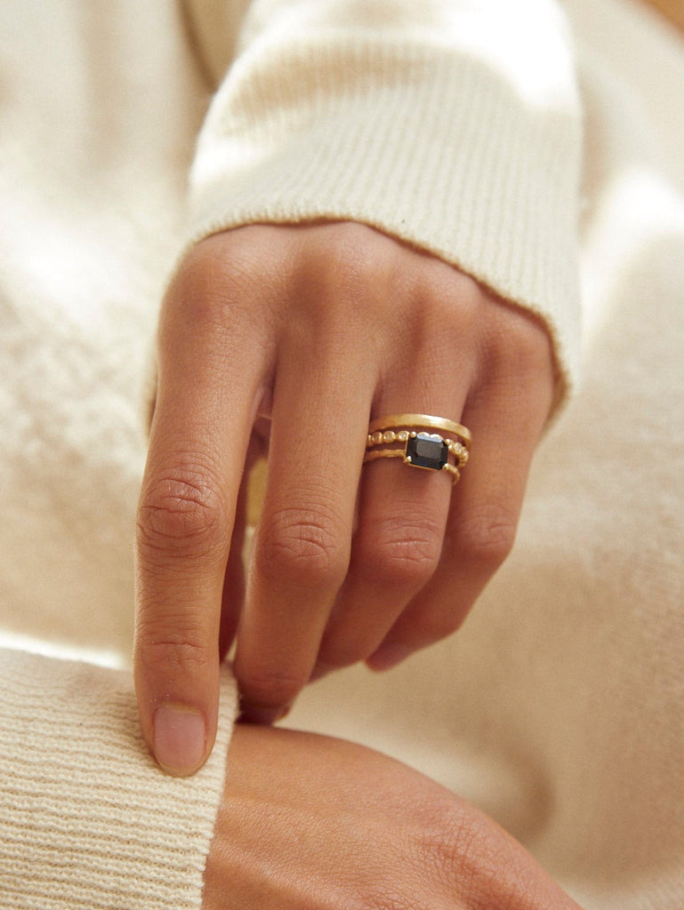 close up of woman wearing gold four prong twig ring with rectangle sapphire alongside other gold rings